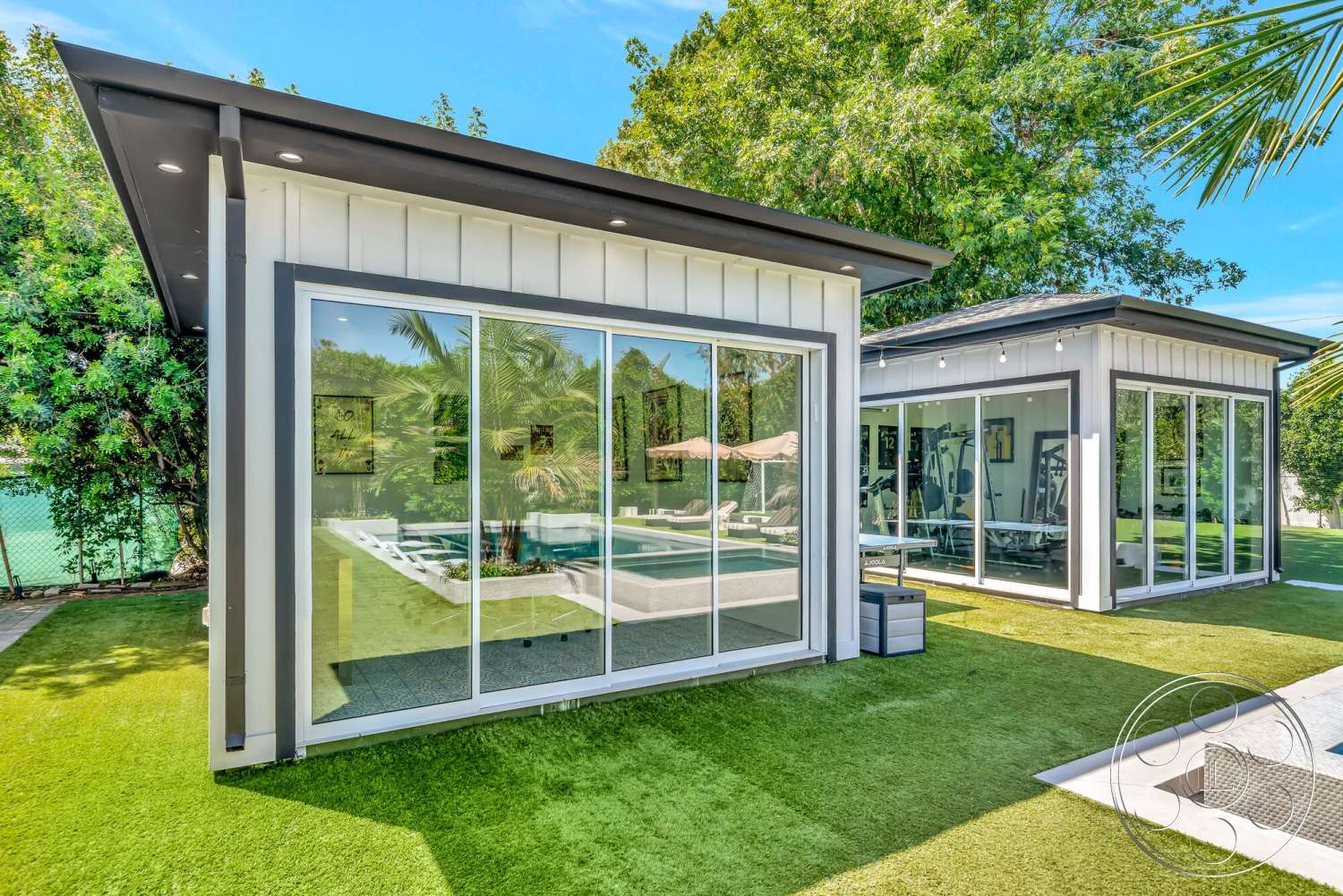 Modern 534 - exterior, modern architectural style, concrete pool deck, metal roof, rectangular pool, large sliding glass doors, glass wall panels, black trim details, artificial turf landscaping, outdoor fitness area, surrounded by tropical greenery, well-lit outdoor space, white exterior finish