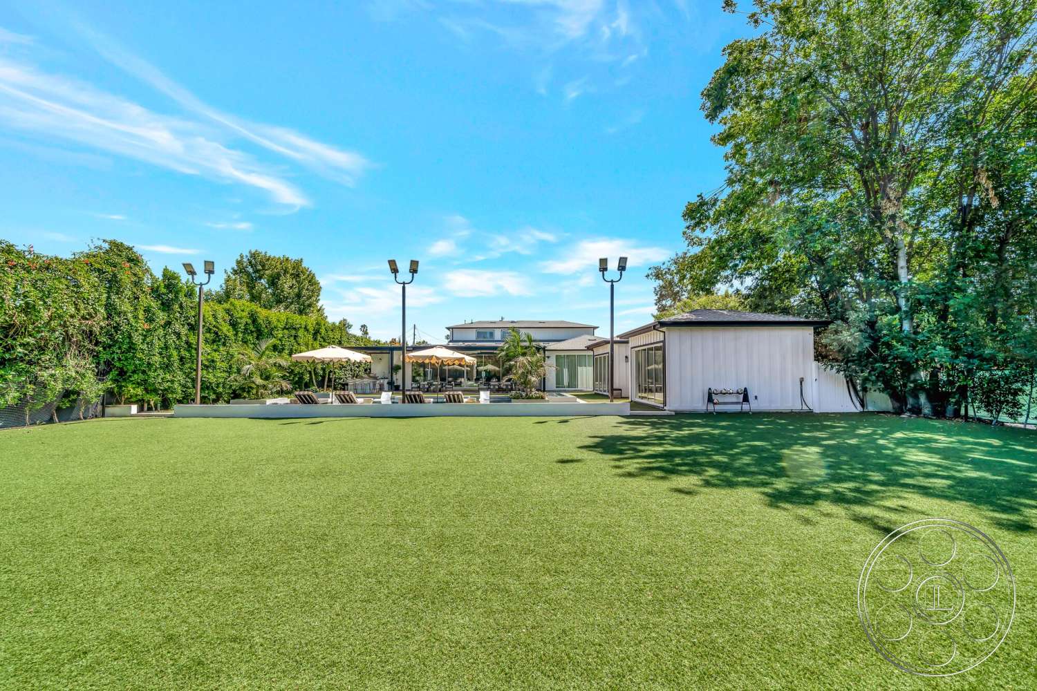 Modern 534 - modern single-story home, concrete patio area, sunny outdoor environment, metal outdoor lighting fixtures, landscaped garden with trees, exterior wall cladding, framed glass sliding doors, pergola with fabric canopy, outdoor lounge area with sun loungers, artificial turf yard