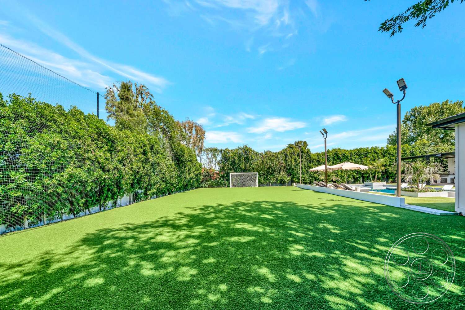 Modern 534 - exterior, lush greenery, sunshade umbrellas, outdoor lighting fixtures, open sky, swimming pool area, flat terrain, artificial grass lawn, soccer goal, landscape hedge fencing, modern backyard setting, patio with lounge chairs