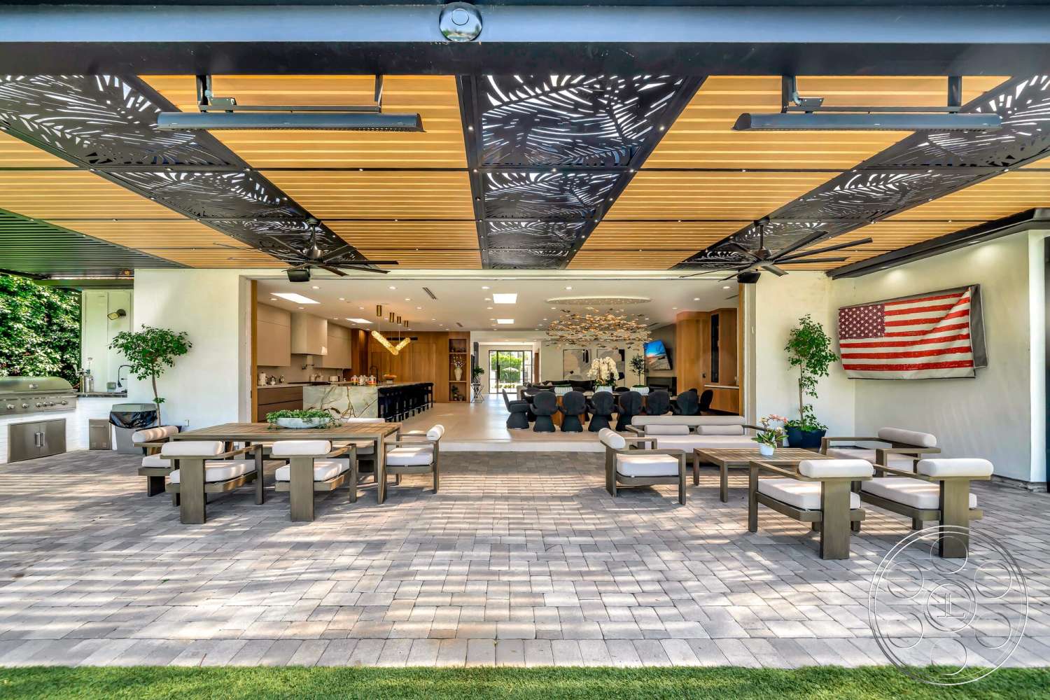 Modern 534 - exterior, open floor plan, wooden dining table, stainless steel grill, landscape greenery, upholstered outdoor seating, contemporary architectural style, wood beam ceiling, paver patio flooring, metal ceiling panels, modern outdoor kitchen, panoramic glass walls, flag wall decoration, sculptural lighting fixture