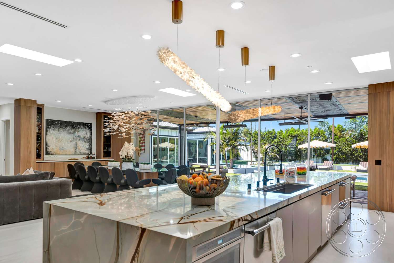 Modern 534 - open floor plan, stainless steel appliances, glass sliding doors, modern aesthetic, artwork on wall, polished tile flooring, exposed ceiling beams, pendant lighting fixtures, contemporary kitchen design, lush green landscaping view, marble kitchen island, wood paneling accent wall, indoor-outdoor living space, luxury dining area, countertop with veined finish, formal dining table with modern chairs, curtained patio enclosure, chandelier style lighting