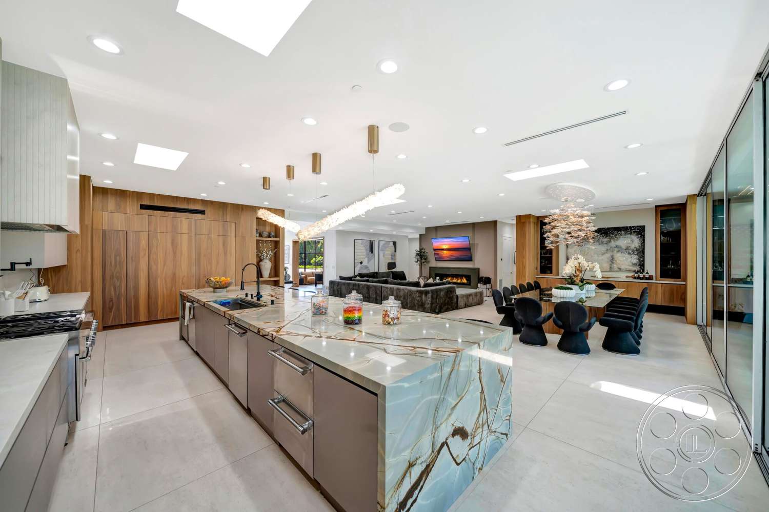 Modern 534 - stainless steel appliances, modern pendant lighting, floor-to-ceiling windows, textured wall paneling, open concept living space, light gray concrete flooring, glass sliding doors leading to outdoor space, minimalist decor with natural elements, round dining table with black chairs, skylights providing natural light, quartz kitchen island with marble pattern, dark hardwood cabinetry, chandeliers with organic design, upholstered sofa in contemporary design, seamless transitions between kitchen and dining area, built-in cabinetry in dining area