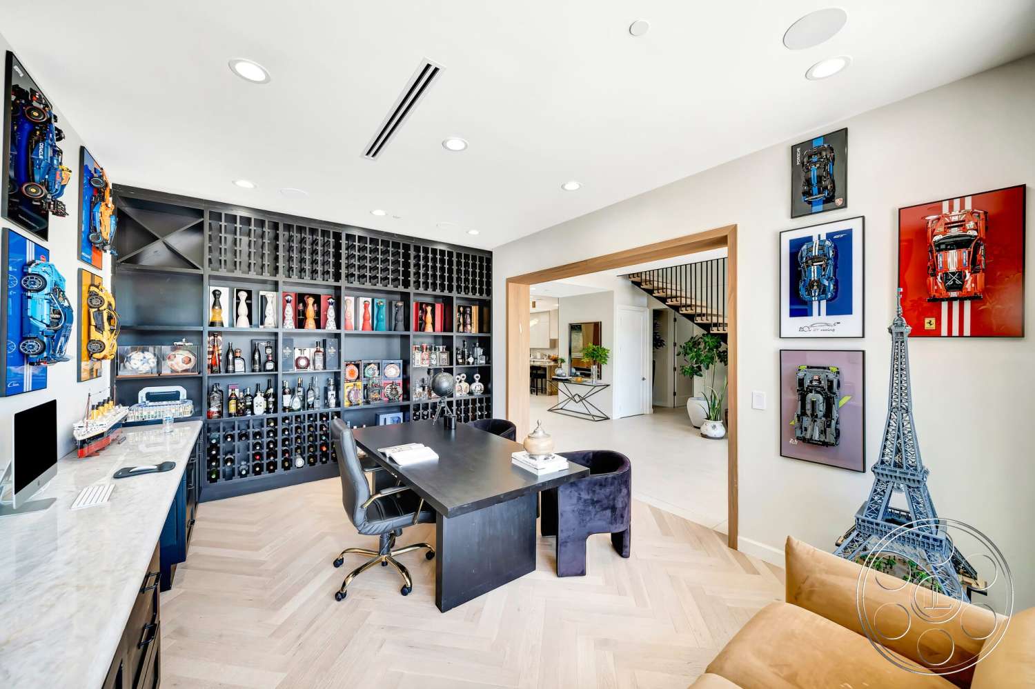 Modern 534 - bright natural lighting, modern decor accents, black dining chairs, neutral painted walls, herringbone hardwood flooring, modern home office, white marble desk surface, gallery wall with framed artwork, black cabinetry with wine storage, exposed metal ceiling fixtures, open doorway leading to adjacent room, multi-color decorative sculptures