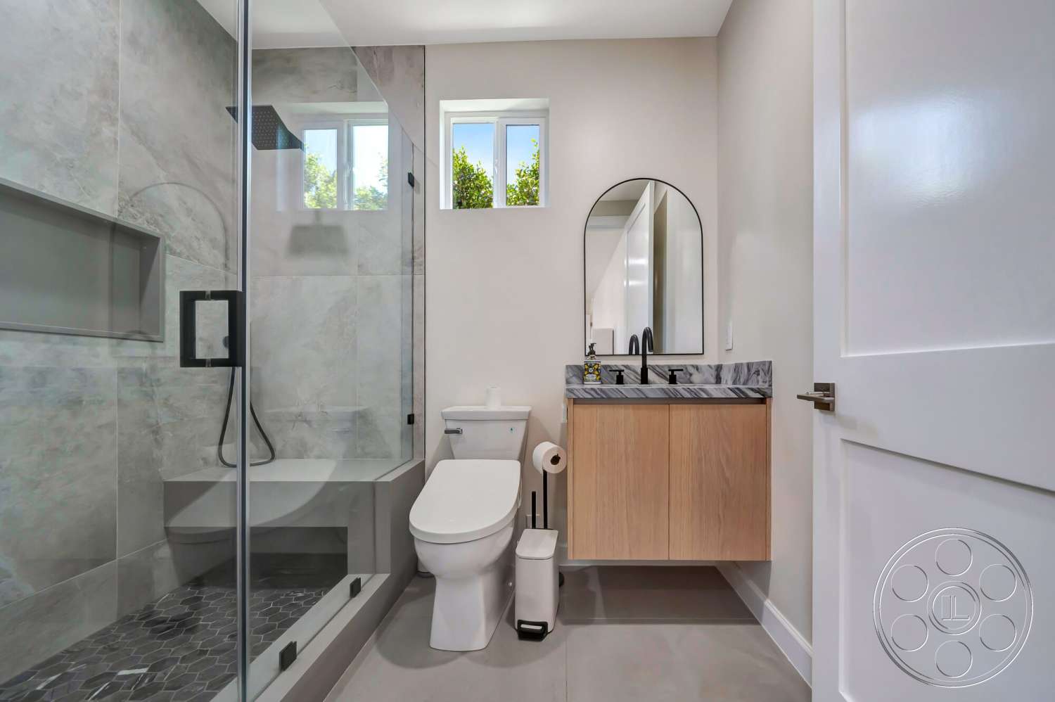 Modern 534 - glass shower enclosure, light wood cabinetry, floor-to-ceiling windows, hexagonal tile flooring, minimalist bathroom design, marble countertop vanity, textured plaster bathroom walls, flush-mounted ceiling lighting, modern oval mirror, black metal faucet