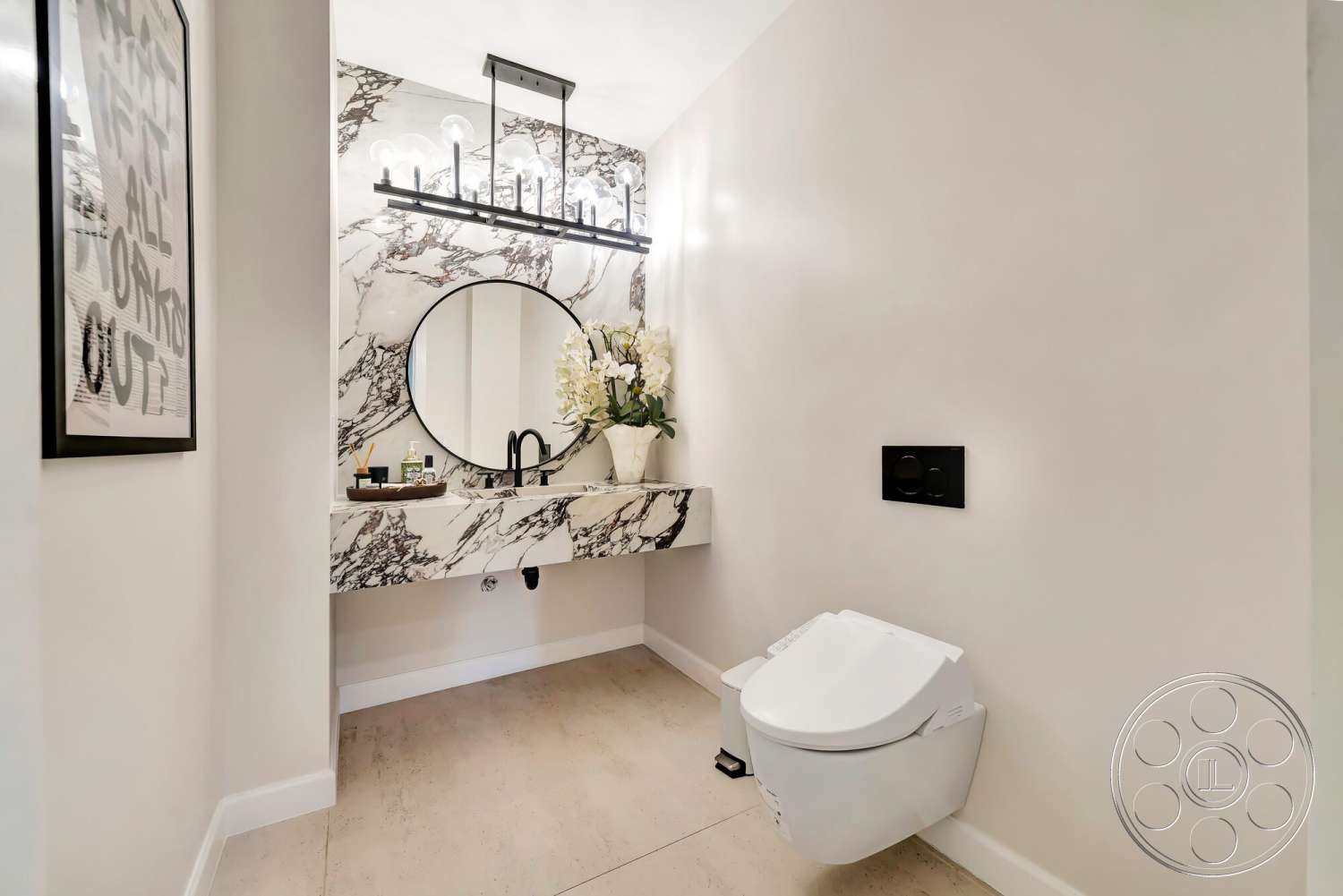 Modern 534 - white painted walls, minimalist toilet design, round mirror with black frame, polished marble bathroom countertop, black metal wall-mounted light fixtures, light beige porcelain tile flooring, black dual flush plate, modern floral arrangement, art print in black frame