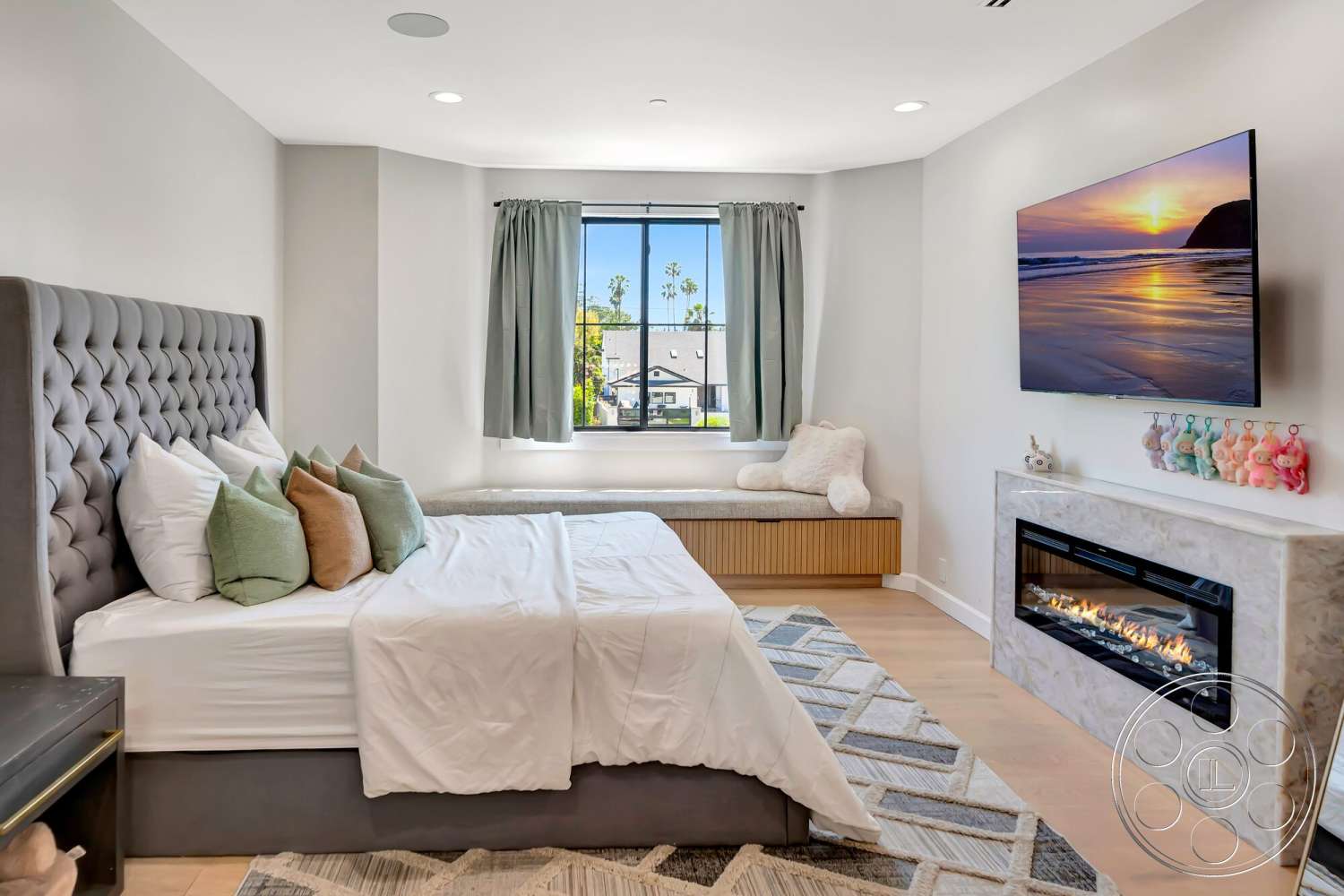 Modern 534 - white bedding, green accent pillows, decorative plush toys, hardwood bedroom floors, modern geometric area rug, upholstered headboard bed, built-in wooden bench, grey tufted bed frame, corner window with white curtains, LED wall-mounted television, white stone fireplace surround