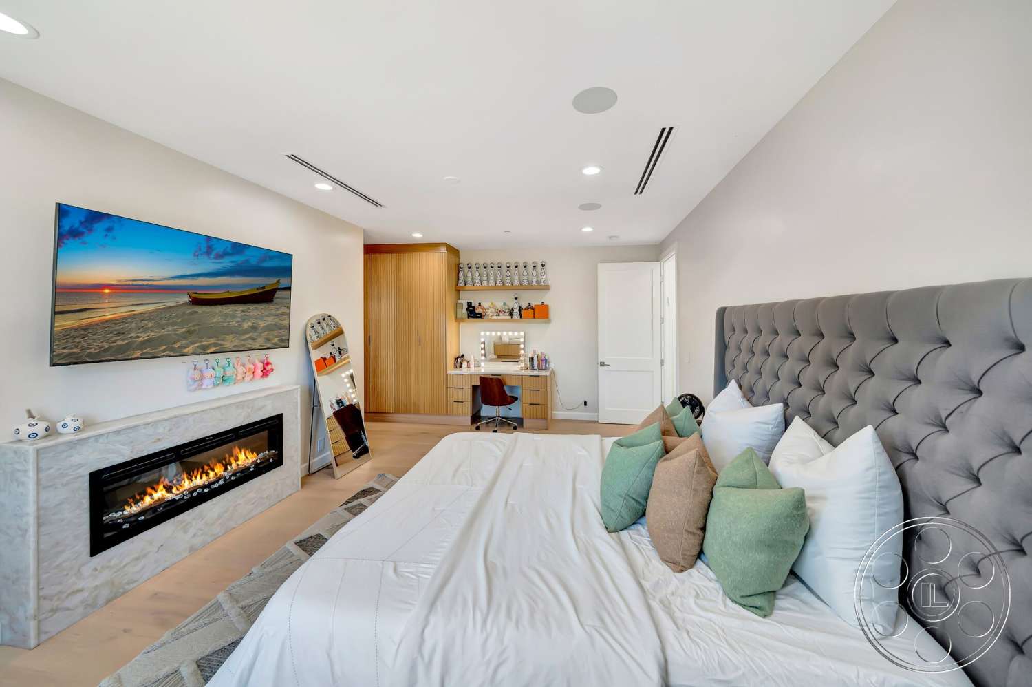 Modern 534 - decorative throw pillows, recessed ceiling lighting, hardwood bedroom floors, integrated ceiling speakers, marble fireplace surround, wall-mounted flat-screen television, tufted gray upholstered headboard, modern wood cabinetry, beige wall paint, minimalist mirror, tiled accent rug