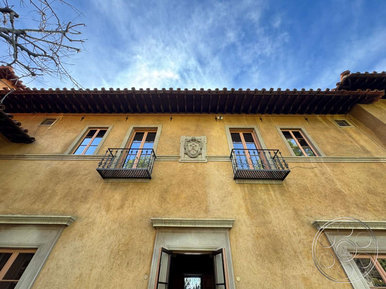Villa Italy - exterior, terracotta roof tiles, metal balcony railings, wooden window frames, traditional architectural style, double-hung windows, stucco wall finish, ornamental stone crest, flat roof eaves, window planter boxes, decorative stone trim, courtyard house setting