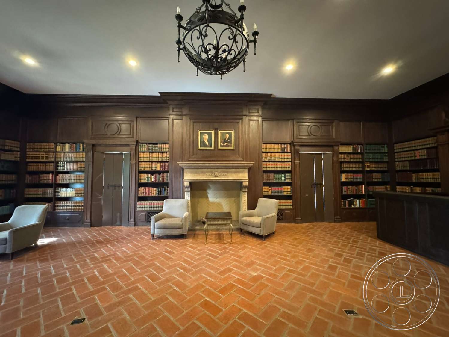 Villa Italy - dark wood doors, dark wood paneling, exposed wood ceiling beams, traditional chandelier lighting, detailed crown molding, built-in bookcases, stone fireplace mantel, painted wall art, brick herringbone flooring, neutral upholstered armchairs, library room