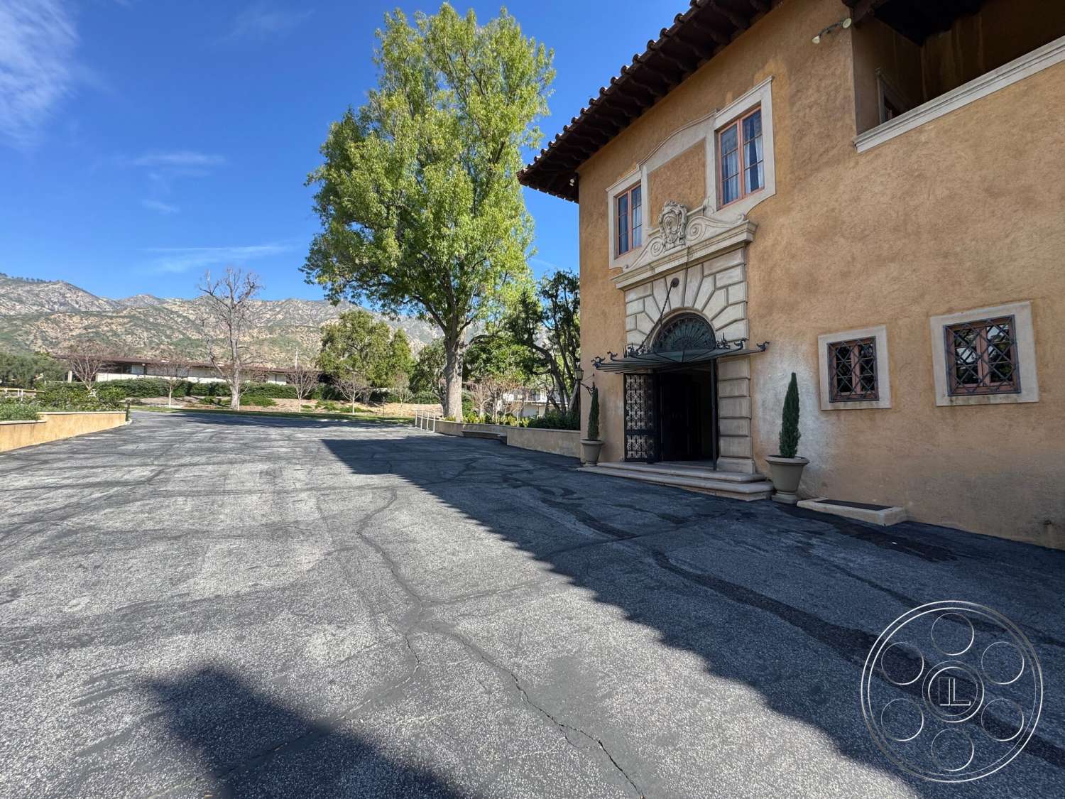 Villa Italy - exterior, symmetrical facade, arched entryway, terra cotta roof tiles, landscape trees, concrete parking lot, stucco building facade, mountain view backdrop, decorative stone trim, granite entrance steps, wooden overhanging eaves, ornate door detail, tapered planters, window with decorative grid