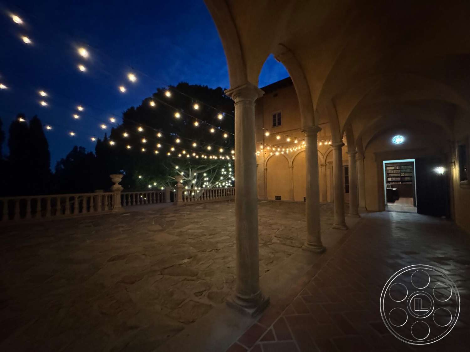 Villa Italy - exterior, landscaped garden view, nighttime ambiance, textured plaster walls, stone patio flooring, arched stone columns, medieval-style architecture, exposed outdoor lighting, porch area with decorative railing