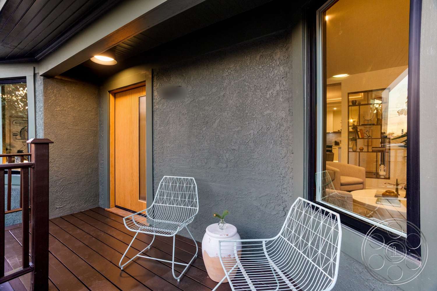 Craftsman 65 - exterior, modern architectural style, floor-to-ceiling window, wooden front door, ceramic planter, metal patio chairs, textured plaster wall, dark wood deck flooring, light fixture on exterior ceiling, brown railing