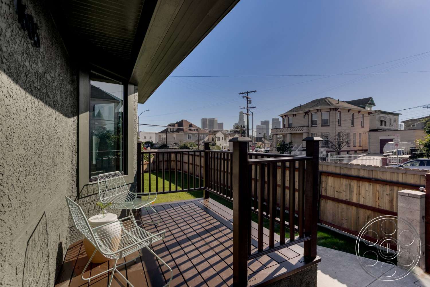 Craftsman 65 - exterior, fenced garden area, floor-to-ceiling windows, sloped roof, city skyline view, textured stucco walls, wood patio flooring, landscaped backyard view, concrete patio surface, wood railing deck, metal wireframe chairs