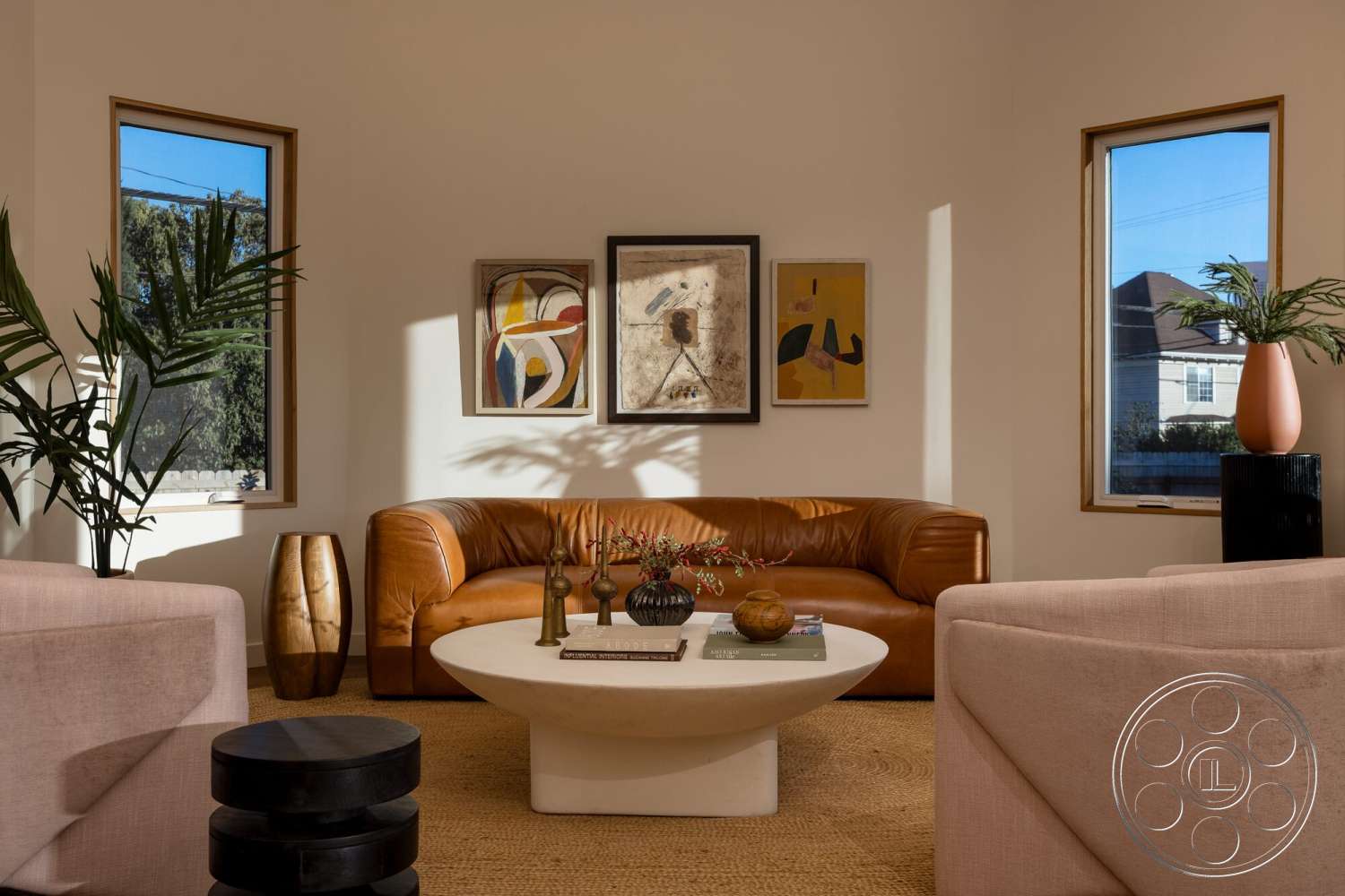 Craftsman 65 - round coffee table, tan leather sofa, painted drywall walls, abstract art wall decor, ceramic decorative bowl, tall indoor plants, wood framed windows, woven jute rug, light pink upholstered armchairs, dark wood vase