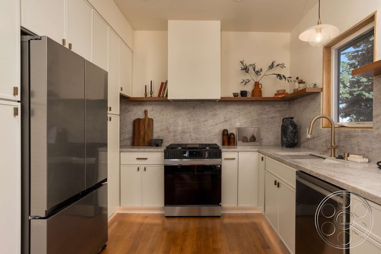Craftsman 65 - neutral color palette, modern pendant lighting, stainless steel refrigerator, natural light from window, interior kitchen, hardwood kitchen flooring, white cabinetry with gold hardware, decorative ceramic vases, dark wood open shelving, black stainless steel stove, light marble kitchen backsplash, double basin kitchen sink, wooden cutting board decor