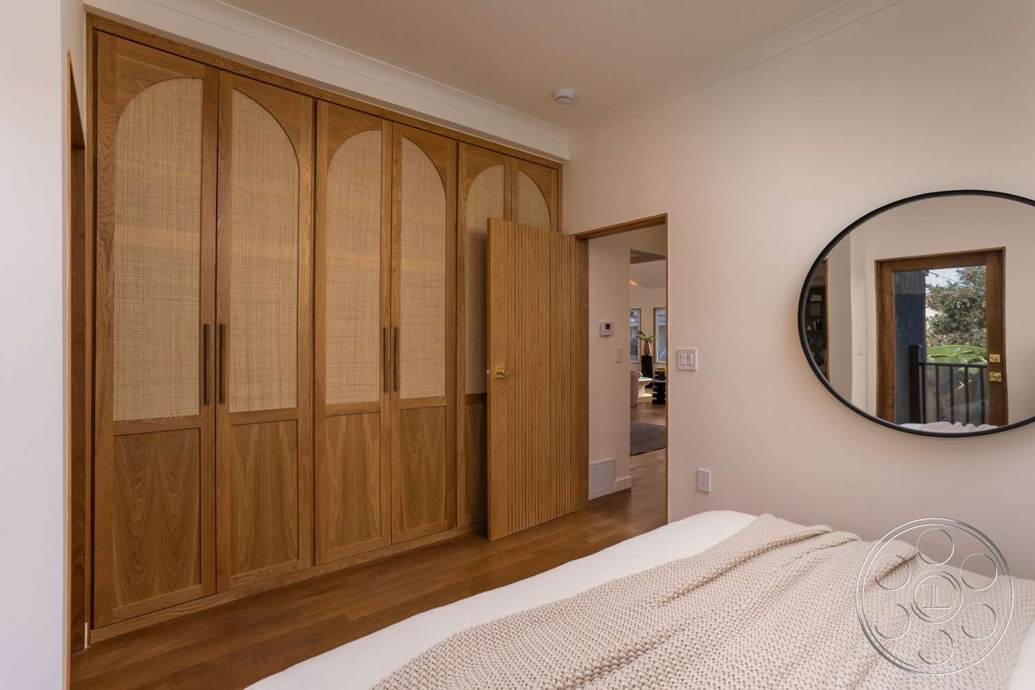 Craftsman 65 - neutral wall colors, natural wood cabinetry, contemporary interior style, modern bedroom design, light hardwood bedroom floors, round mirror with black frame, open doorway leading to adjacent room, woven cane cabinet doors, arched cabinet door shapes