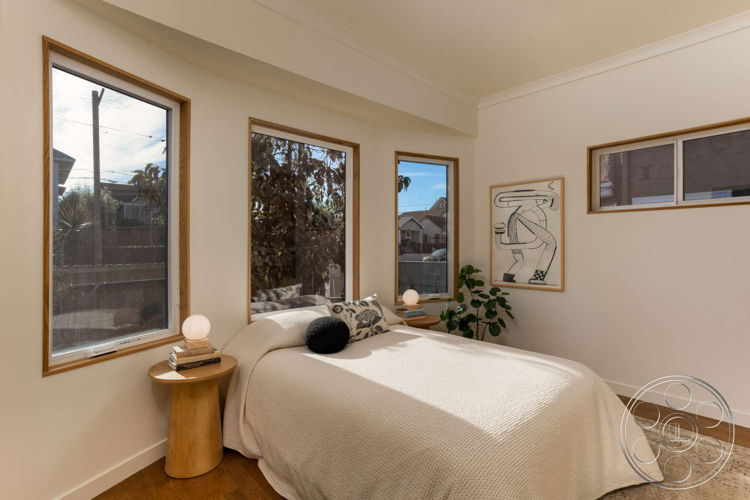 Craftsman 65 - accent wall art, hardwood bedroom floors, large windows with natural light, potted indoor plant, minimalist bedroom design, light-colored painted walls, natural wood window frames, round wood side table, white bedspread, geometric shapes in decor
