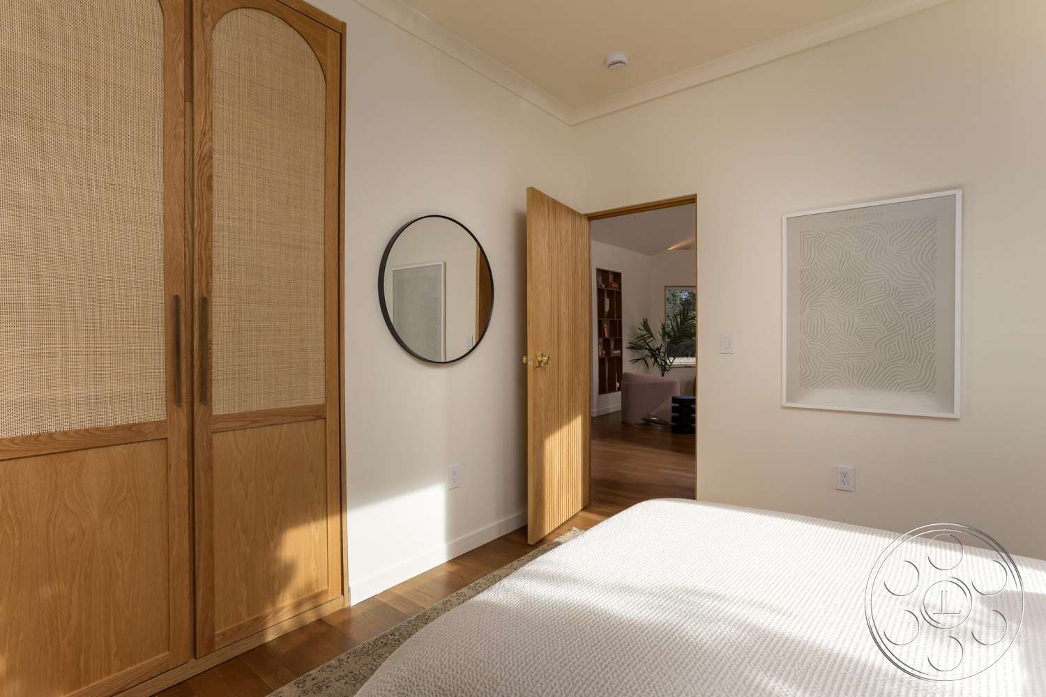Craftsman 65 - textured area rug, arched door frame, hardwood bedroom floors, minimalist artwork on wall, light-colored painted walls, round mirror with black frame, wood sliding door with woven cane panels