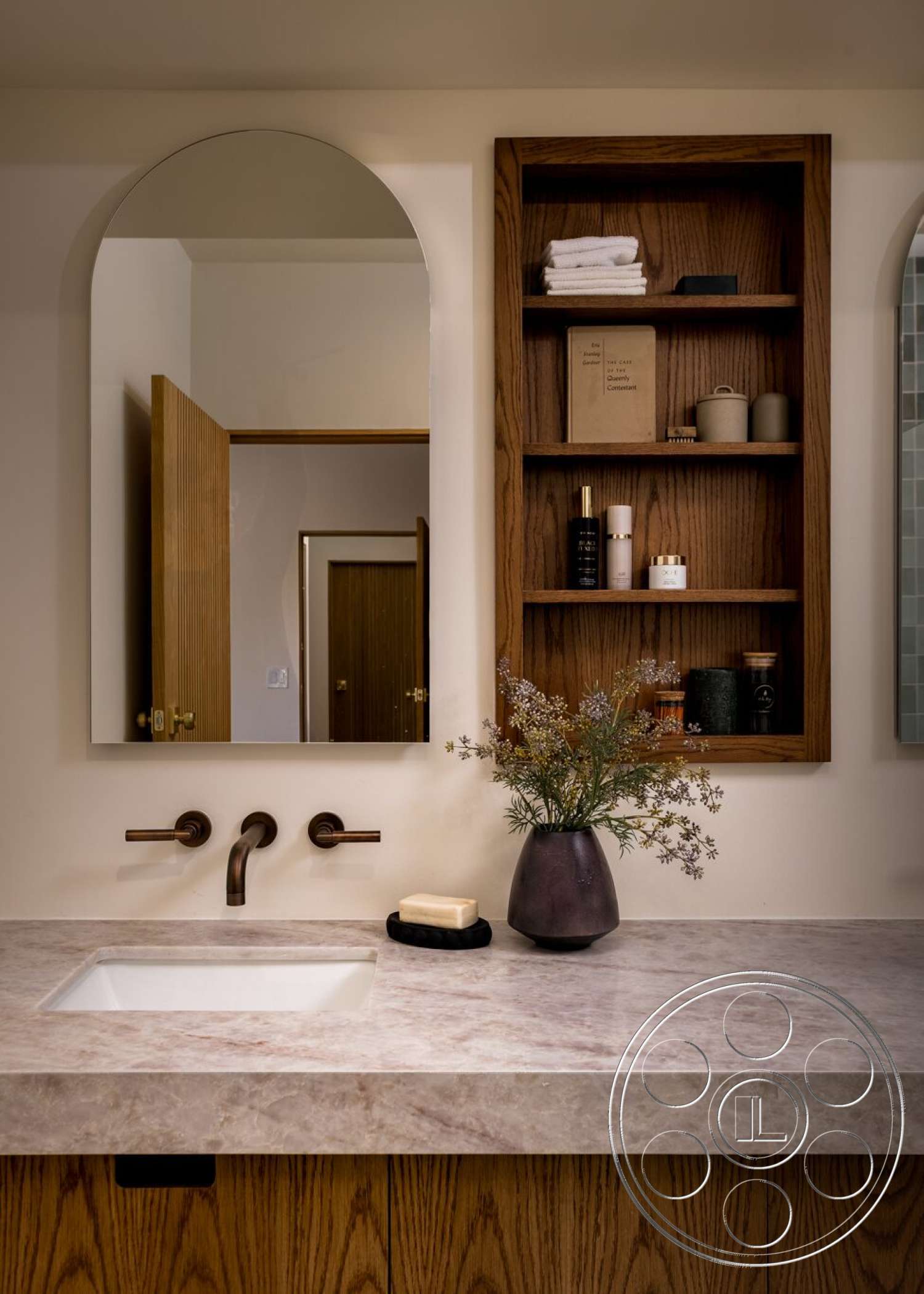 Craftsman 65 - wood cabinetry, textured wall treatment, white quartz countertop, undermount sink, arched mirror, decorative vase with flowers, minimalist bathroom decor, beige painted walls, soft towel arrangement, bronze faucet fixtures, bathroom storage solutions, oak wood shelves, flooring tiles