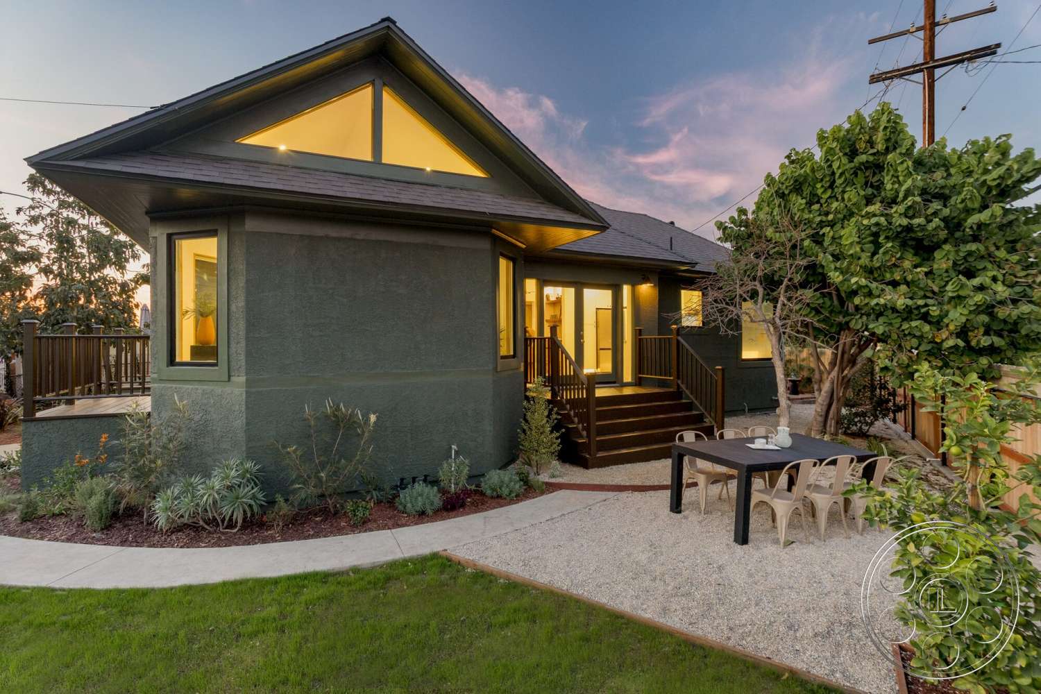 Craftsman 65 - exterior, concrete pathway, large floor-to-ceiling windows, green stucco walls, outdoor dining table, landscaped garden area, gravel patio flooring, wooden deck stairs, decorative shrubbery, pitched roof with overhang, geometric roof shape