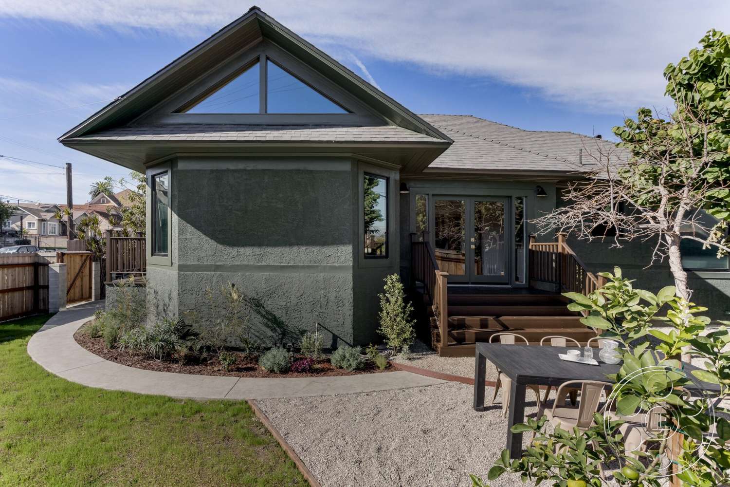 Craftsman 65 - exterior, asphalt shingle roof, sliding glass doors, outdoor dining area, lush green lawn, modern residential architecture, rectangular patio area, stucco wall finish, landscaped garden beds, concrete patio border, wooden fence enclosure, wooden deck stairs, rounded pathway design, large triangular windows, low-maintenance gravel landscaping, dining table setting
