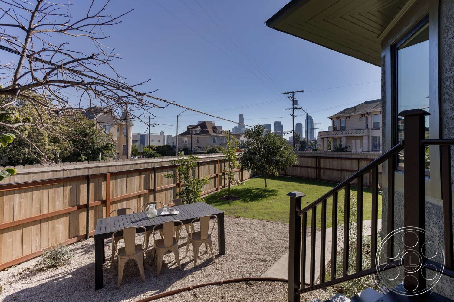 Craftsman 65 - exterior, city skyline view, wooden fence, landscape greenery, metal dining chairs, gravel patio flooring, green lawn area, contemporary home design, rectangular outdoor dining table, steps leading to backyard