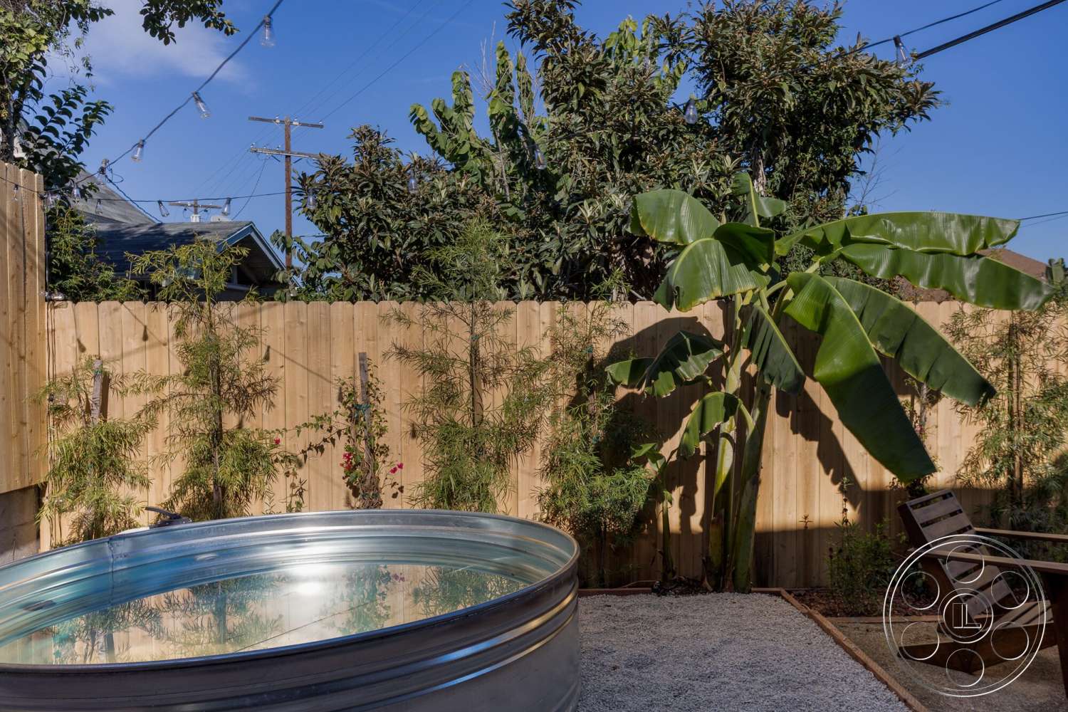 Craftsman 65 - exterior, outdoor seating area, bamboo plants, string lights, tropical landscaping, natural sunlight, wooden privacy fence, gravel patio flooring, galvanized steel pool, banana tree