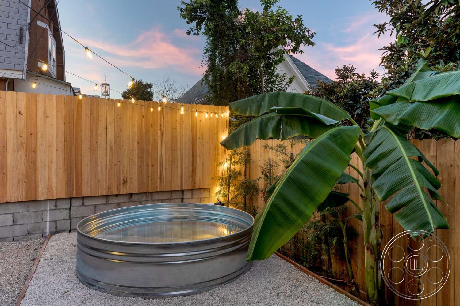 Craftsman 65 - exterior, brick wall, string lights, wooden fence, landscaped garden area, gravel patio flooring, cedar wood fence panels, galvanized steel fire pit, tropical banana plant, small outdoor space