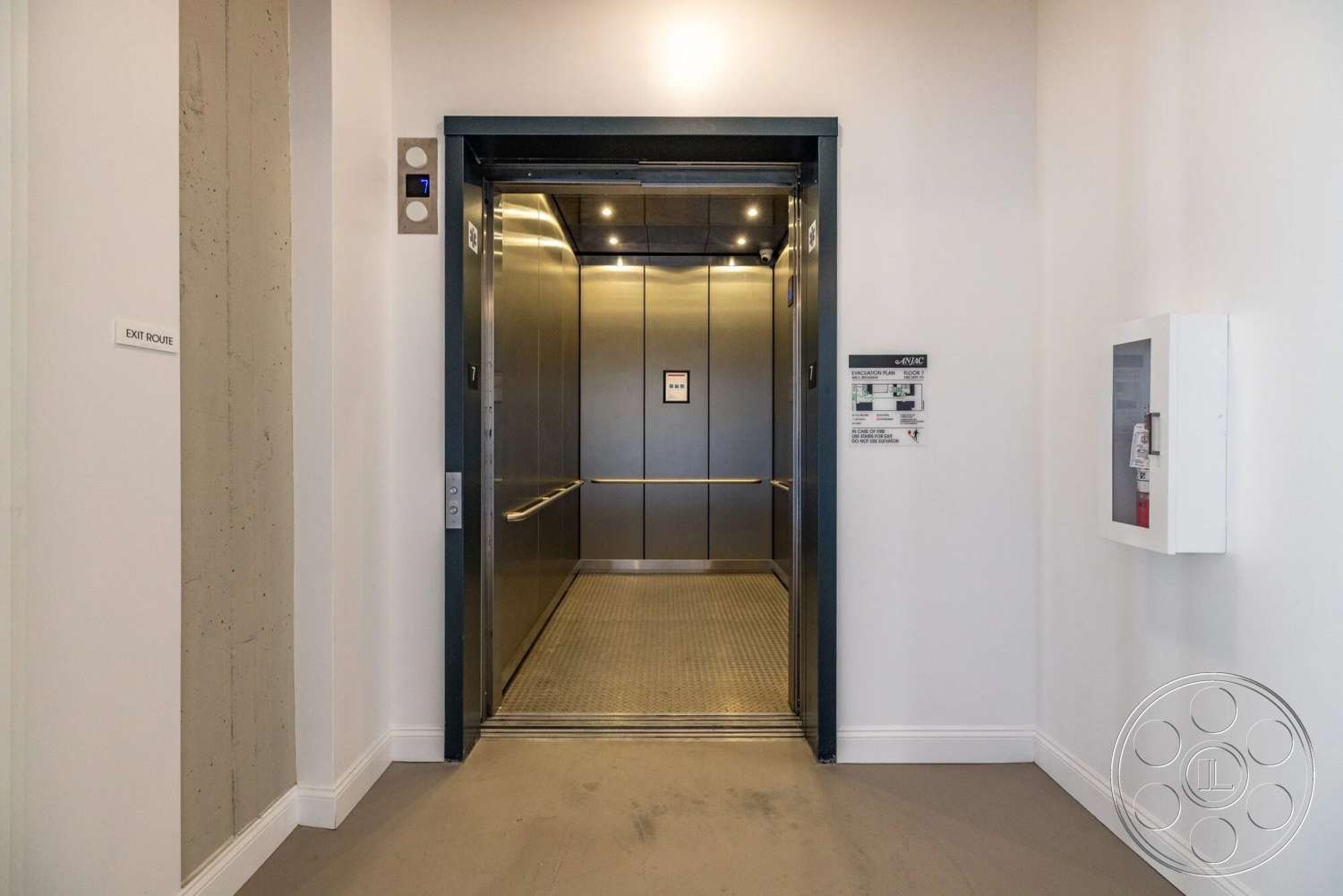 Loft 1 - lighting fixtures, white painted walls, metal elevator doors, minimalist wall paneling, modern elevator design, concrete accent wall, signage details, composite flooring, exit route signage
