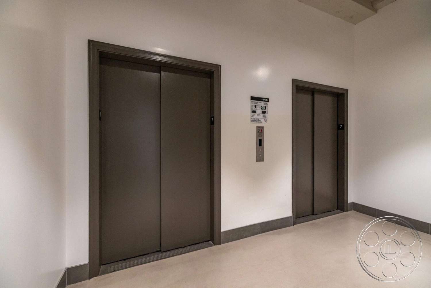 Loft 1 - ambient lighting, smooth concrete flooring, white painted walls, minimalist architectural design, metal elevator doors, interior elevator lobby, modern elevator button panel, gray tile base trim
