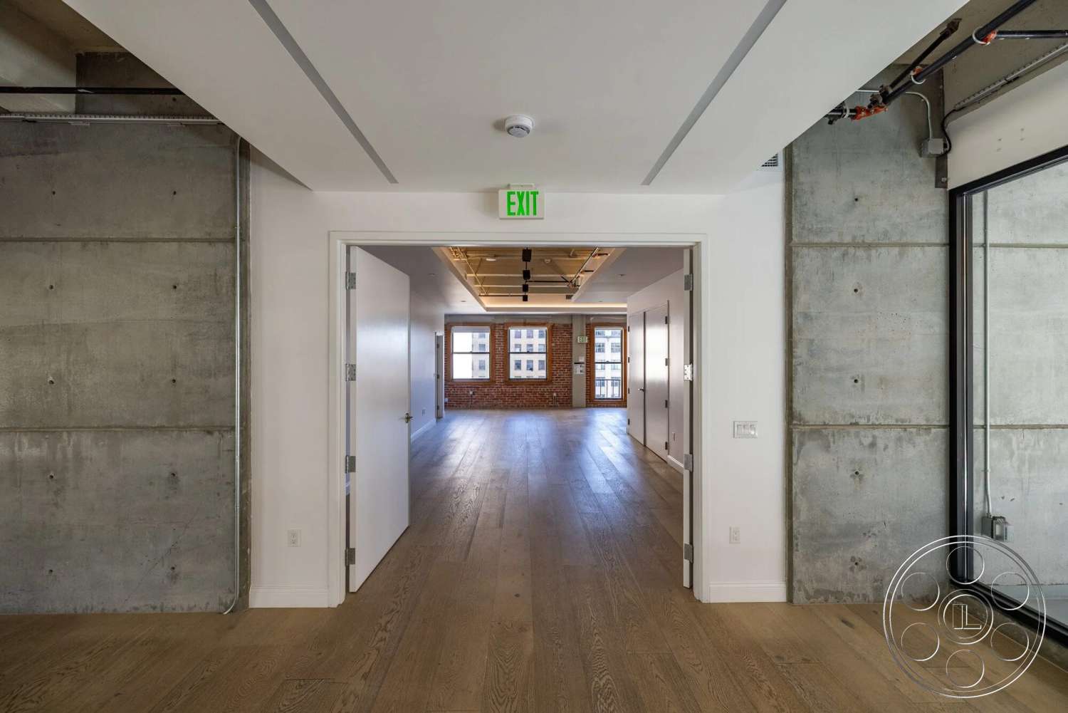 Loft 1 - open floor plan, concrete walls, floor-to-ceiling windows, exposed concrete, red brick accent wall, white painted walls, modern recessed lighting, wide plank hardwood flooring, straight hallway, minimalist door designs