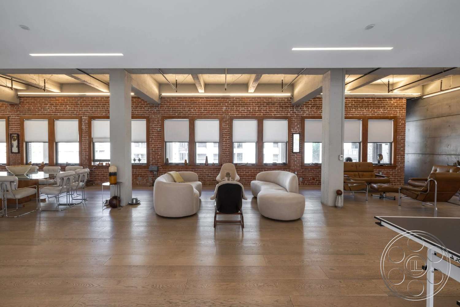 Loft 1 - open floor plan, leather armchairs, modern dining table, ambient ceiling lighting, polished hardwood flooring, exposed brick interior walls, concrete ceiling beams, contemporary decor elements, urban loft style, steel window frames, large windows with roller shades, minimalist sofa seating