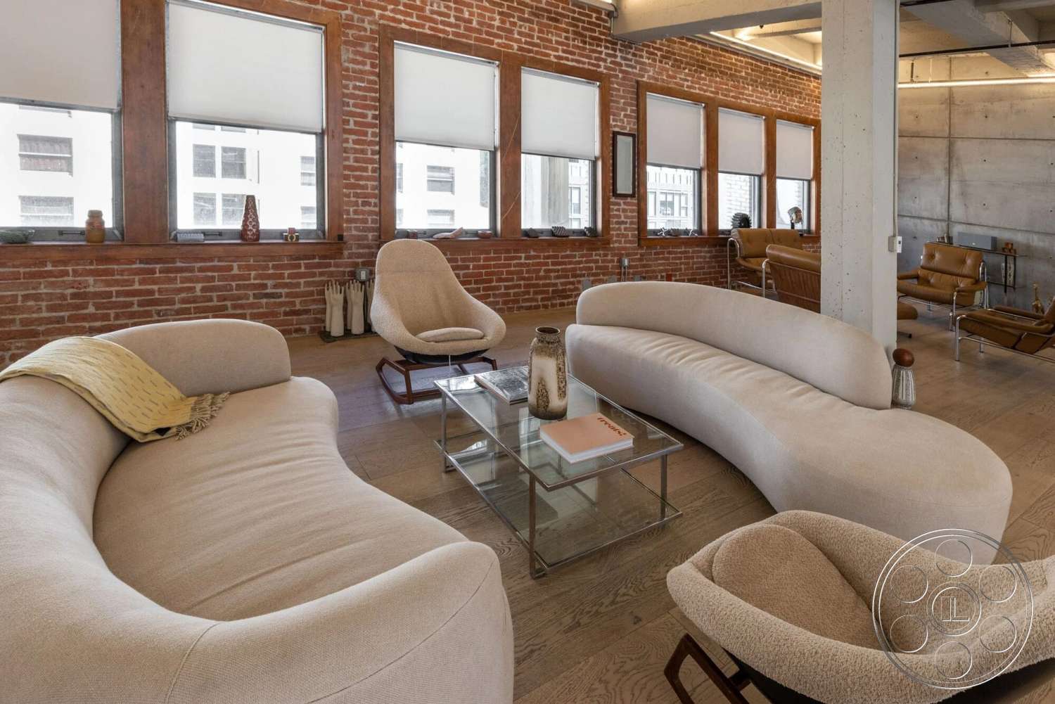 Loft 1 - hardwood flooring, plush armchair, concrete ceiling, metal coffee table, curved sectional sofa, open concept living area, exposed brick accent wall, industrial style architecture, natural light-filled interior, large windows with blinds
