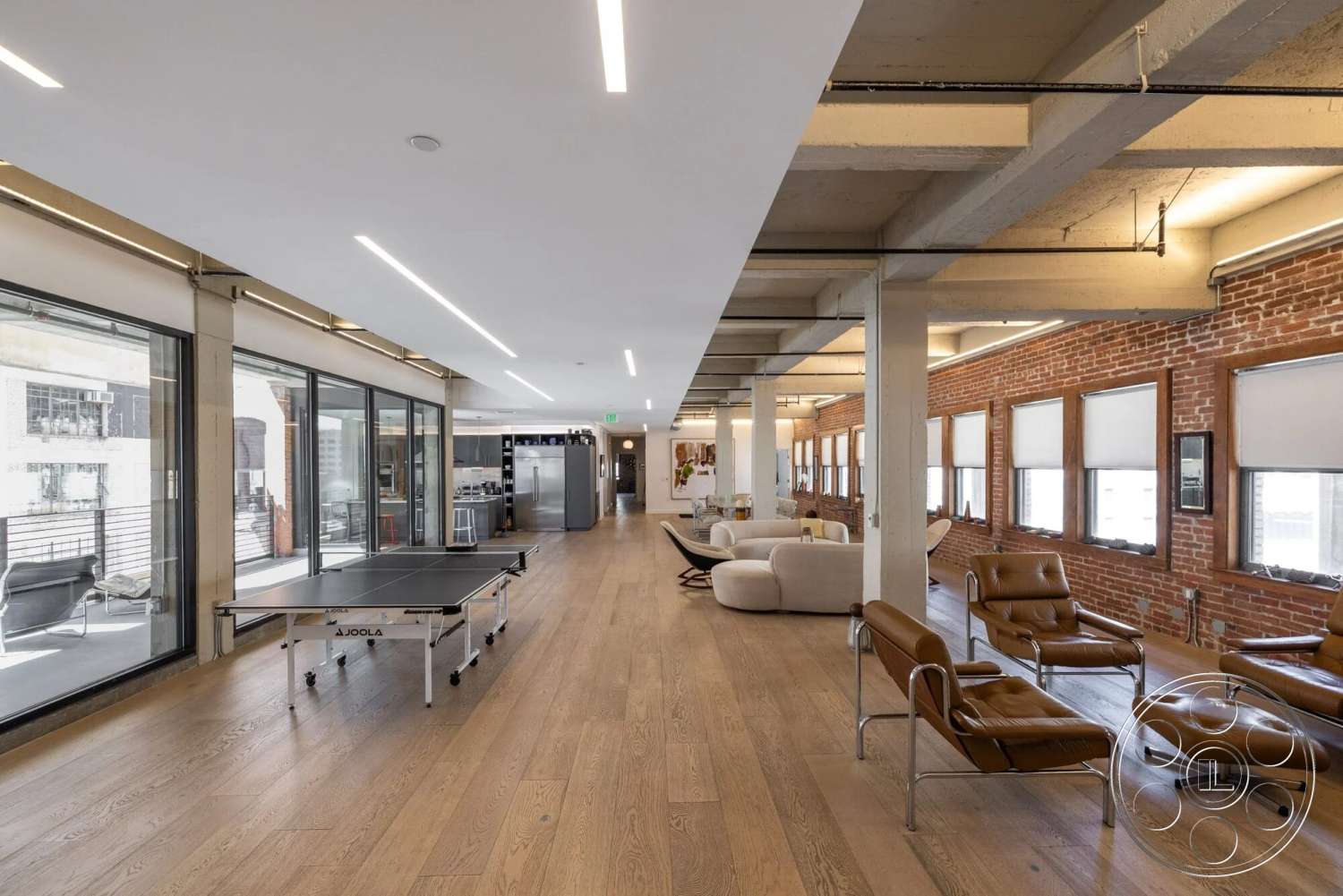 Loft 1 - hardwood flooring, contemporary furniture, open concept layout, exposed brick walls, floor-to-ceiling windows, linear LED lighting, concrete ceiling, modern lounge area, ping pong table, steel structural columns, urban loft setting, overhead ductwork