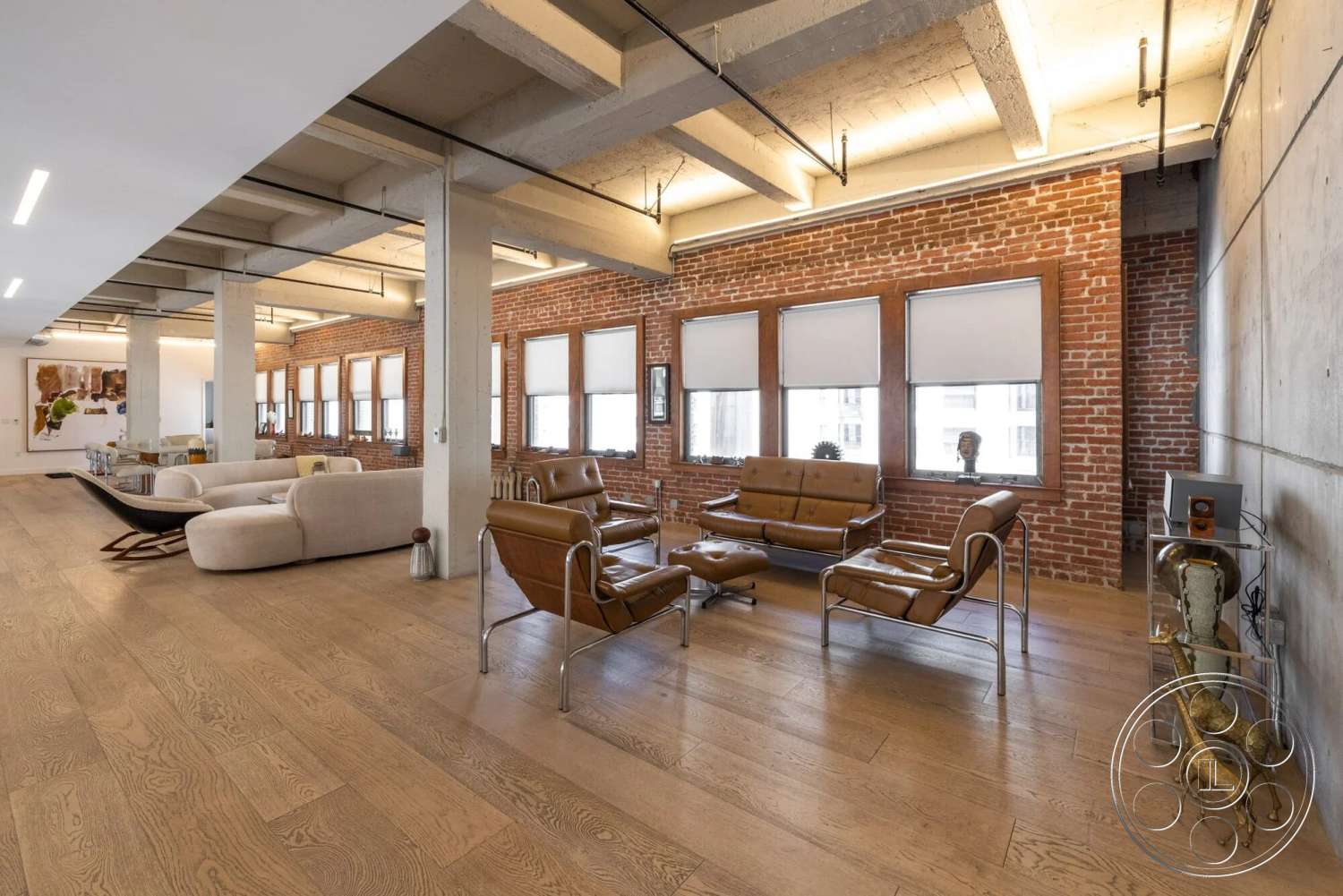 Loft 1 - hardwood flooring, open floor plan, exposed brick walls, floor-to-ceiling windows, industrial lighting fixtures, bright interior, contemporary art on walls, textured plaster walls, urban loft setting, concrete ceiling beams, modern leather seating, windows with wood trim, exterior view of cityscape