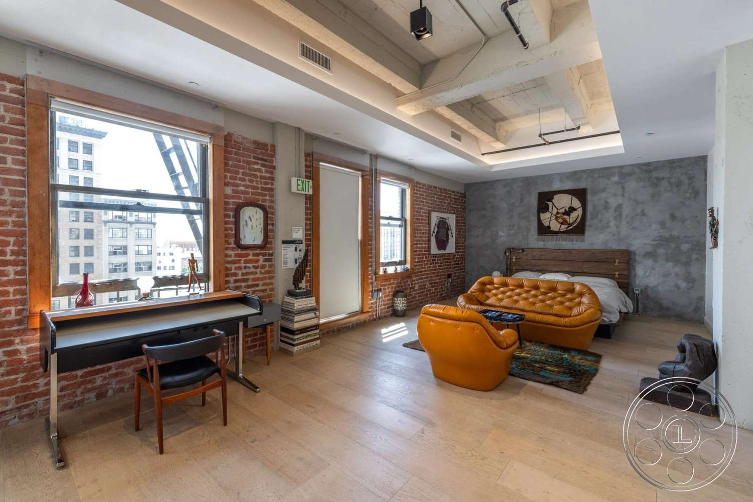 Loft 1 - contemporary artwork, floor-to-ceiling windows, textured plaster wall, hardwood bedroom floors, exposed brick accent wall, open urban setting, concrete ceiling with exposed beams, modern leather tufted armchair, wood frame bed with tufted headboard, metal desk with wooden top