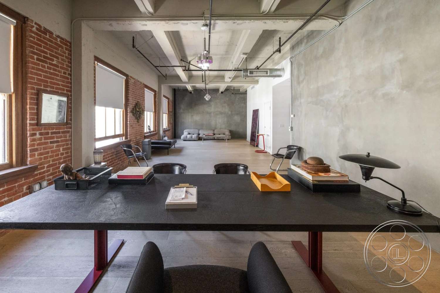 Loft 1 - modern pendant lighting, concrete walls, urban setting, floor-to-ceiling windows, hardwood floor, rectangular table, open layout design, natural light exposure, exposed brick accent wall, white painted ceiling, contemporary office decor, minimalist workspace, industrial style office, metal desk legs