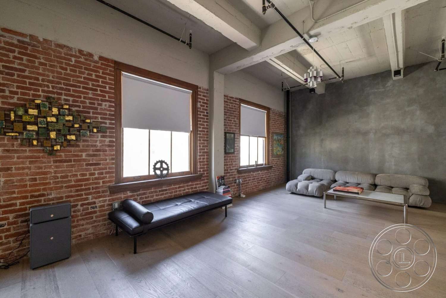 Loft 1 - minimalist decor, floor-to-ceiling windows, metal coffee table, hardwood living room floors, natural light illumination, modern sectional sofa, exposed brick accent wall, open concept interior, smooth plaster wall, industrial ceiling beams