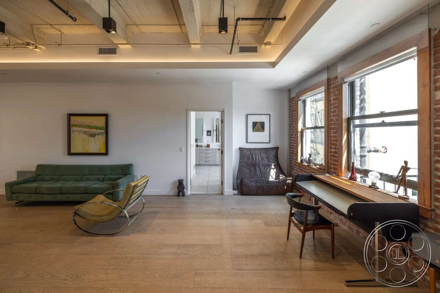Loft 1 - artistic wall decor, exposed brick walls, light hardwood floors, mid-century modern accent chair, white painted walls, large windows with metal frames, concrete ceiling with exposed beams, modern sectional green sofa, minimalist wooden desk