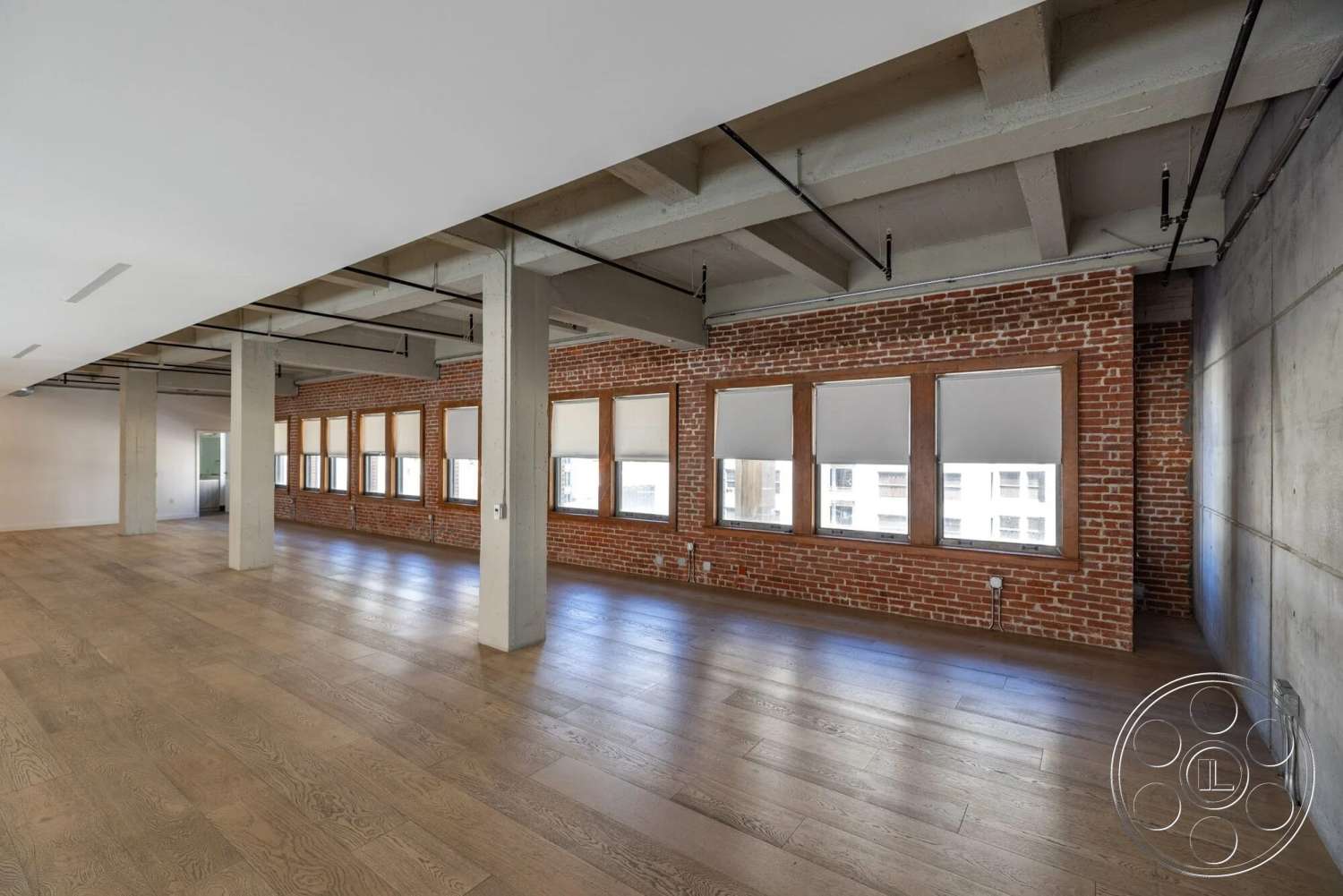 Loft 1 - hardwood flooring, open floor plan, floor-to-ceiling windows, modern minimalist design, natural light-filled space, white painted walls, steel support columns, exposed brick accent wall, industrial style interior, concrete ceiling beams