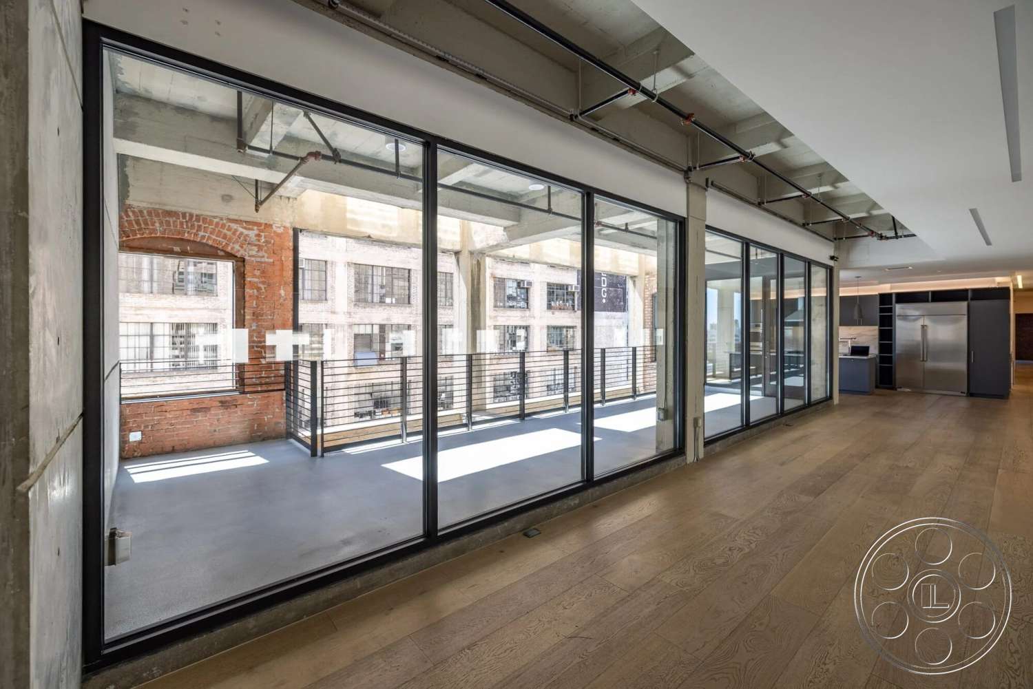 Loft 1 - large glass sliding doors, open floor plan, steel railing, concrete ceiling, modern industrial design, hardwood living room floors, exposed brick accent wall, urban loft interior, kitchen area with stainless steel appliances