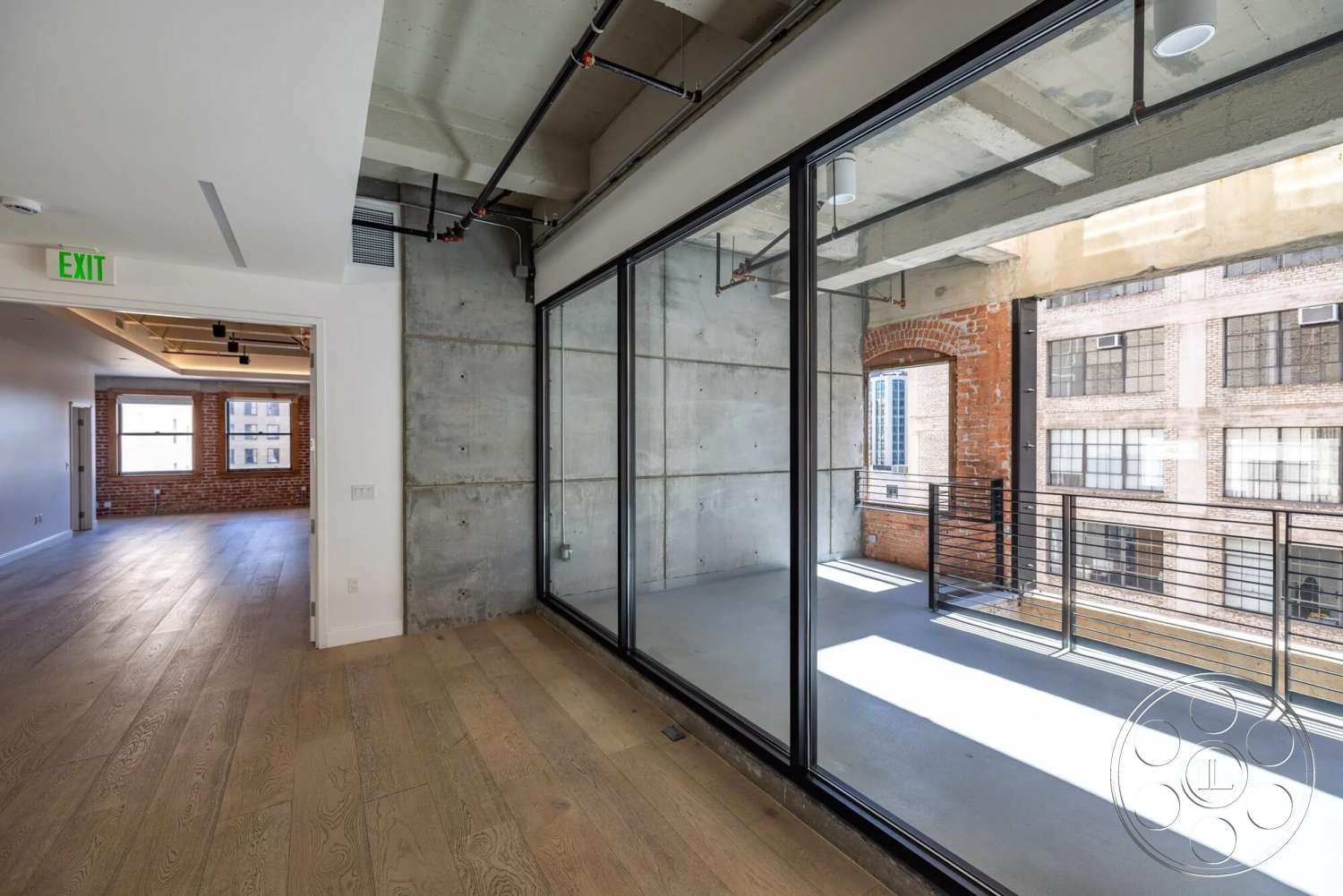 Loft 1 - large windows, natural light, hardwood flooring, open floor plan, glass sliding doors, exposed concrete walls, urban setting, brick accent wall, exposed ceiling beams, metal balcony railing, interior industrial style, modern balcony space