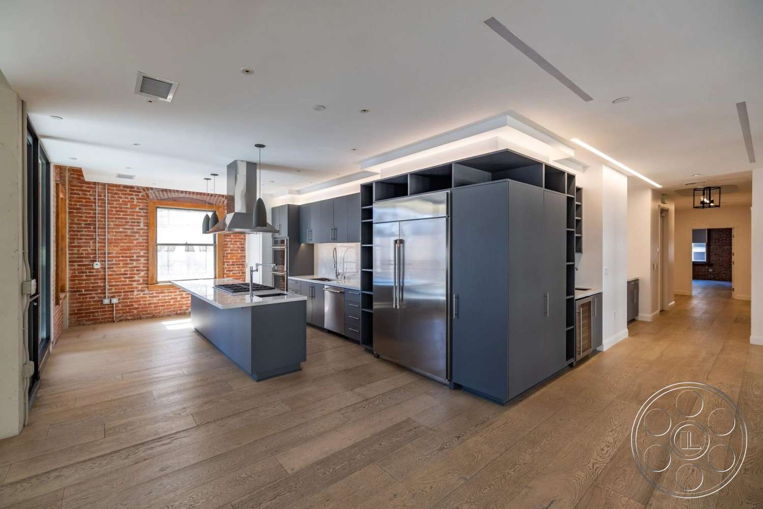 Loft 1 - hardwood flooring, open floor plan, stainless steel appliances, dark cabinetry, contemporary pendant lighting, industrial style, floor-to-ceiling windows, modern kitchen island, polished countertop, exposed brick accent wall, linear recessed lighting, built-in kitchen storage