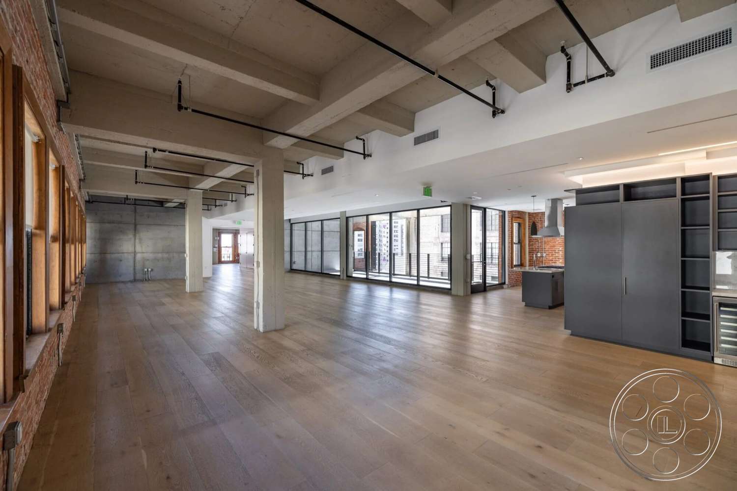 Loft 1 - hardwood flooring, open floor plan, concrete block walls, industrial style, floor-to-ceiling windows, black cabinetry, exposed brick accent wall, concrete ceiling beams, commercial loft space
