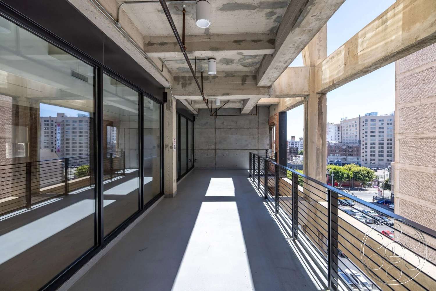 Loft 1 - exposed concrete walls, urban skyline view, concrete ceiling, floor-to-ceiling glass windows, steel support beams, metal railing details, industrial architectural style, concrete balcony floor, open-air exterior space