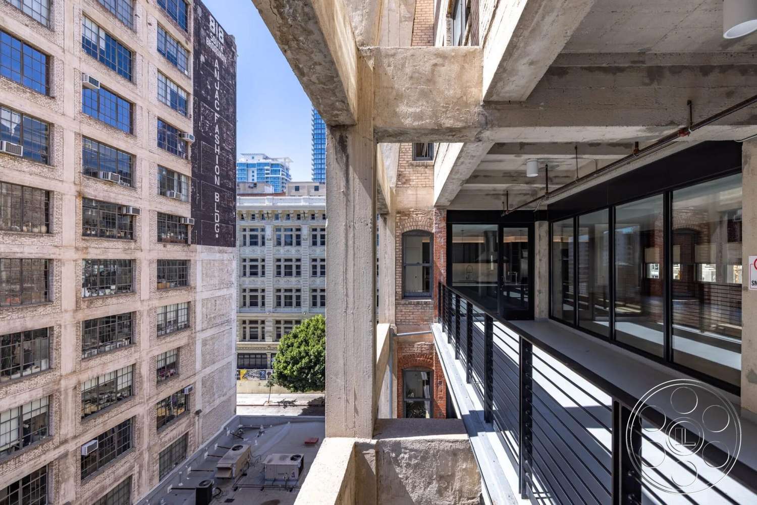 Loft 1 - exterior, urban setting, large industrial windows, brick accent wall, steel railing, historic building, glass partition walls, open-air corridor, concrete balcony floor, exposed concrete beams, modern loft aesthetic, factory-style architecture