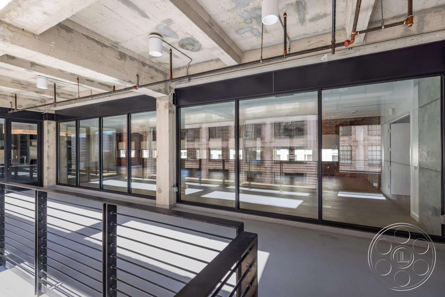Loft 1 - open floor plan, polished concrete flooring, concrete walls, urban setting, black metal railing, exposed concrete ceiling, floor-to-ceiling glass windows, steel support beams, modern architectural design, industrial style interior