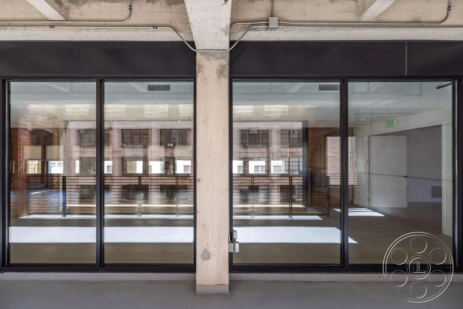 Loft 1 - open floor plan, large glass windows, exposed concrete walls, urban setting, smooth concrete flooring, exposed ceiling beams, industrial style architecture, brick accent walls, steel window frames