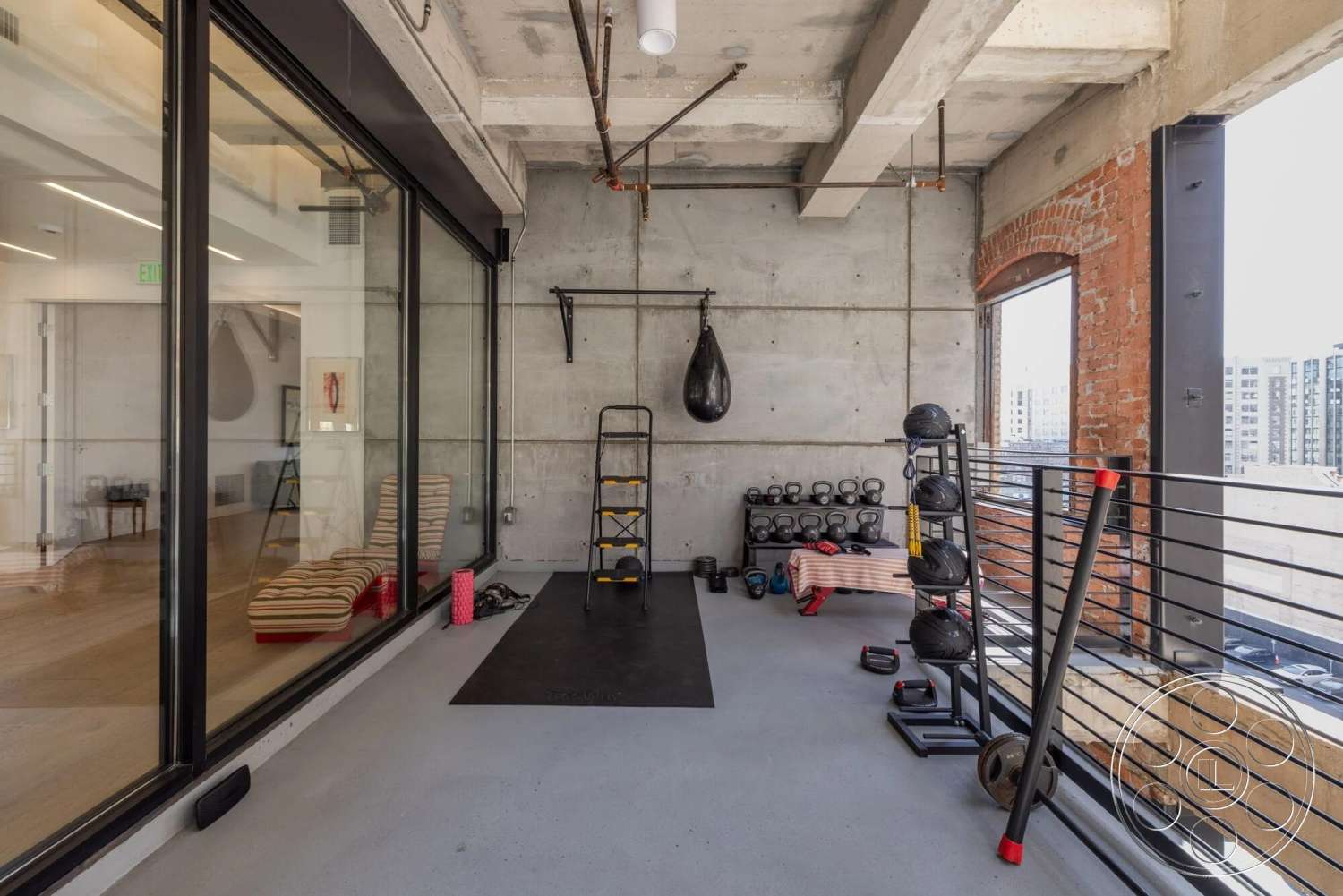 Loft 1 - concrete flooring, exposed concrete walls, metal railing, floor-to-ceiling windows, brick accent wall, fitness room, industrial-style interior, open layout space, modern gym equipment, boxing area