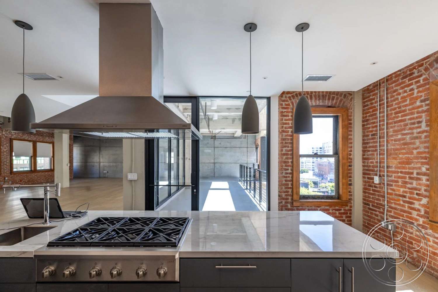 Loft 1 - modern kitchen, concrete walls, floor-to-ceiling windows, hardwood floor, exposed ceiling beams, pendant lighting fixtures, marble kitchen countertops, stainless steel range hood, open-concept interior design, brick kitchen accent wall